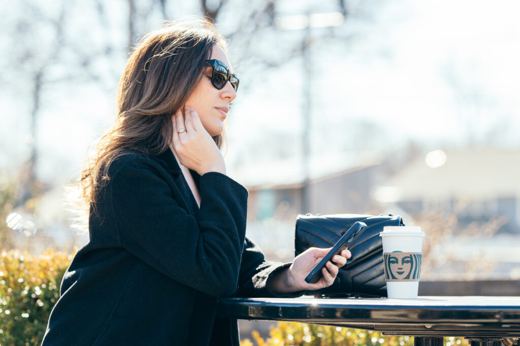 lifestyle portrait of a young woman with an yves saint laurent purse, starbucks coffe and an Iphone